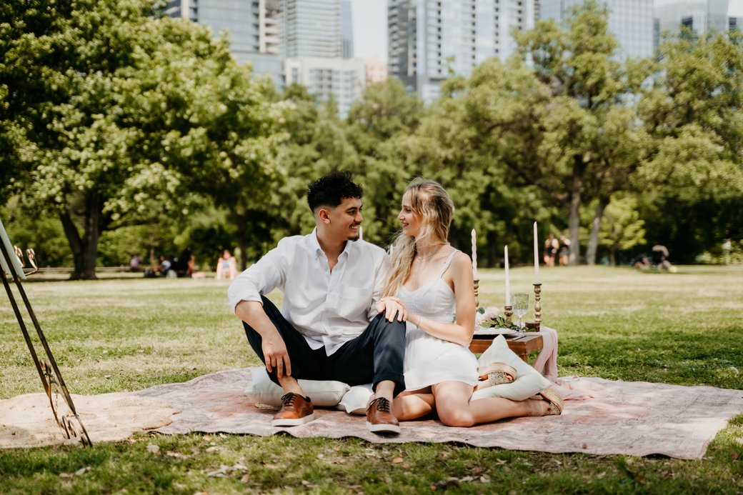 Brandon and Elena, founders of Morning Muse, on a blanket in a park with the Atlanta skyline behind them