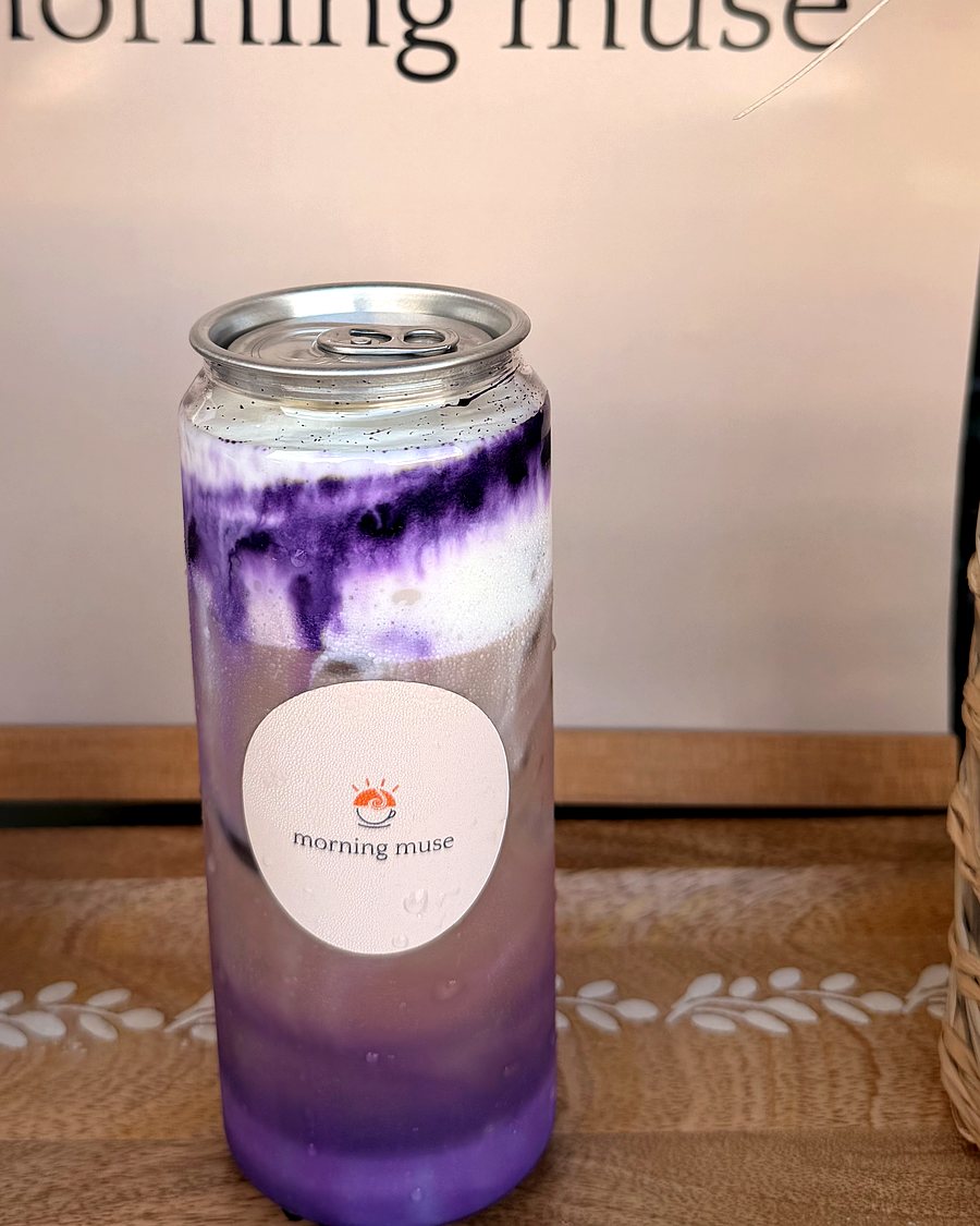Ube latte in a Morning Muse can, deep purple layered through milk over ice, on the branded backdrop